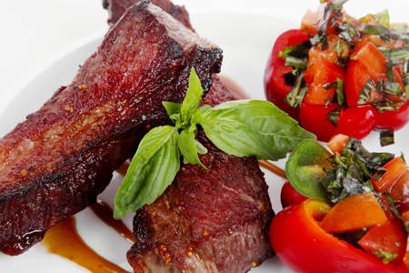 fresh red beef meat steak barbecue garnished vegetable salad and basil  in half of pepper bell on white plate isolated over white backgroundの写真素材