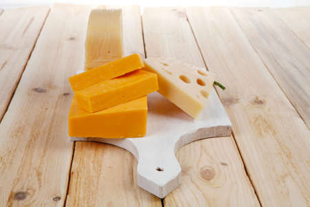 various types of fresh raw aged delicatessen cheese on white plate over light wooden table cheddar edam swissの写真素材