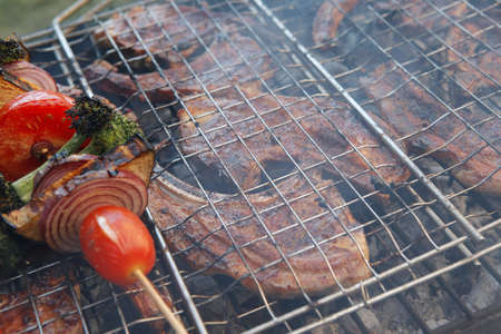 fresh raw lamb ribs on meat holder over fire burned churcoal with vegetable shish kebab on side...