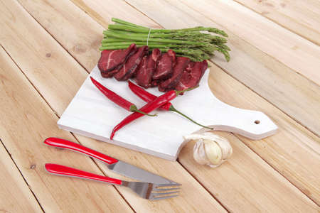 fresh beef meat slices asparagus spices cutlery wooden table pepper hot chili vegetables served garlic light cutting board ready to cookの写真素材