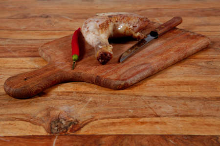 grilled chicken thighs on wooden cut board and red hot chili pepper and stainless steel knife over light wooden tableの写真素材