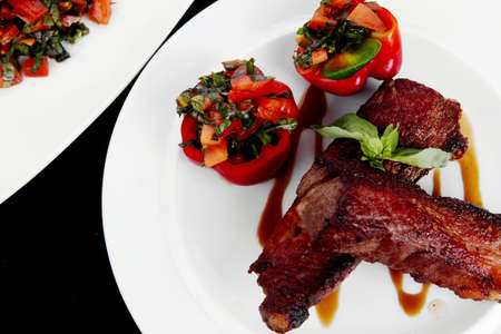 fresh red beef meat steak barbecue garnished vegetable salad and basil on white plate over black wooden table with bbq sauce in sauceboatの写真素材