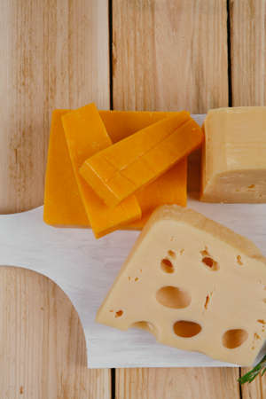 various types of fresh raw aged delicatessen cheese on white plate over light wooden table cheddar edam swissの写真素材