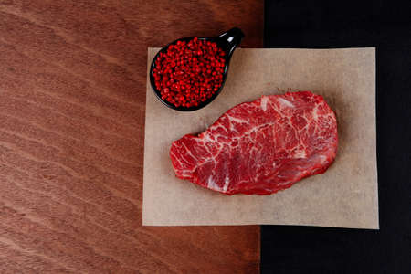 fresh raw beef rib eye steak on black walnut wooden table with red hot pepper spice in saucerの写真素材