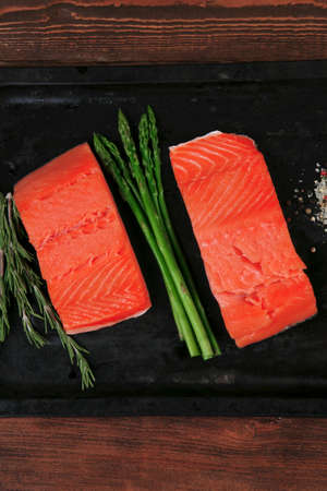two piece of fresh raw pink salmon on black tray with rosemary and asparagus dry spices healthy food diet cooking conceptの写真素材