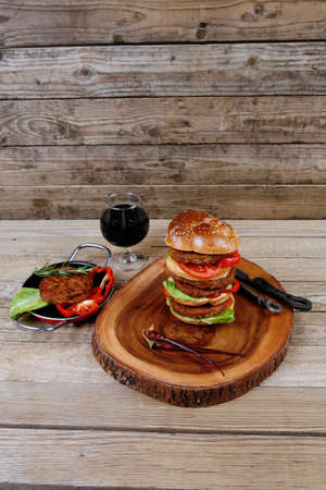 fresh grilled beef huge hamburger served on wood plate with red wine glass chili pepper rosemary green salad leaf and forged vintage antique cutlery over wooden table empty space for textの写真素材
