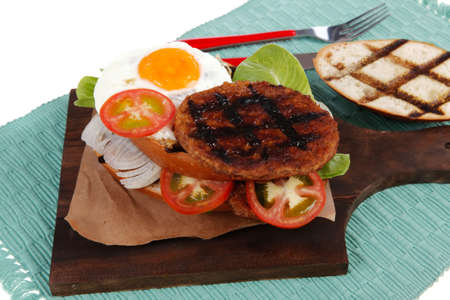 junk food big beef hamburger on dark wood plate with modern cutlery on blue mat isolated over white backgroundの写真素材