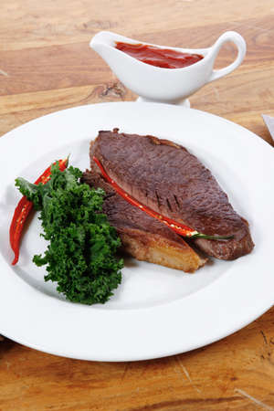 grilled beef steak fillet meat with red hot pepper and  raw kale leaf with ketchup sauce served on white plate over wood tableの写真素材