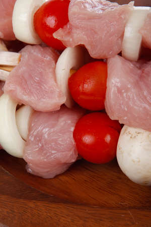 fresh raw meat fillet shish kebab turkey pork pink on skewers tomatoes mushrooms on wooden dish isolated over white backgroundの写真素材