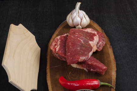 fresh raw beef piece fillet on middle size wooden plate with pepper and peppercorns in measuring...