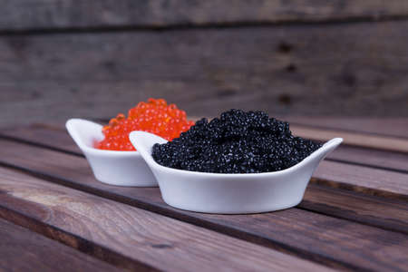 black sturgeon hausen caviar with red salmon caviar in white bowls on wooden backgroundの写真素材