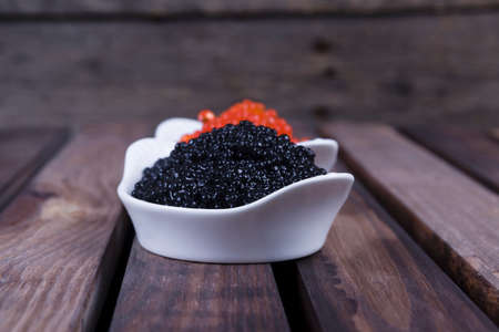 black sturgeon hausen caviar with red salmon caviar in white bowls on wooden backgroundの写真素材