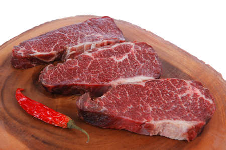 three fresh raw marble beef meat sirloin porterhouse steak on big wooden cutting plate with hot chili pepper isolated on white backgroundの写真素材