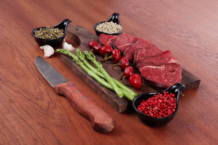 fresh beef meat asparagus greenery spices cutlery wooden table pepper crushed hot chili vegetables bowl served garlic cutting boardの写真素材