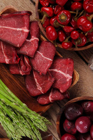 fresh beef meat asparagus greenery spices cutlery wooden table pepper crushed hot chili vegetables bowl servedの写真素材