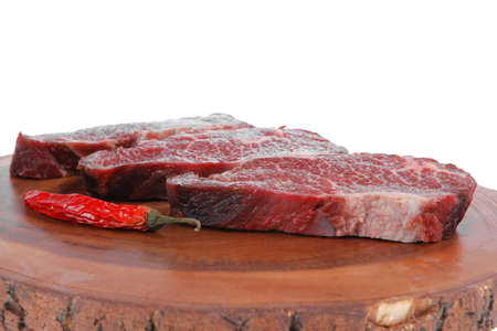 three fresh raw marble beef meat sirloin porterhouse steak on big wooden cutting plate with hot chili pepper isolated on white backgroundの写真素材