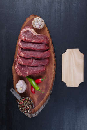 fresh raw beef pieces fillet on big size wooden plate with pepper and peppercorns in measuring spoon name plate space for text on black backgroundの写真素材