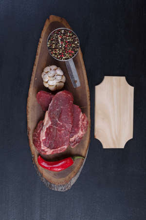 fresh raw beef piece fillet on middle size wooden plate with pepper and peppercorns in measuring spoon with name plate space for text on black backgroundの写真素材