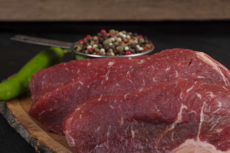 fresh raw beef piece fillet on middle size wooden plate with pepper and peppercorns in measuring spoon space for text on black backgroundの写真素材