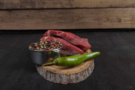 fresh raw beef piece fillet on middle size wooden plate with pepper and peppercorns in measuring spoon space for text on black backgroundの写真素材