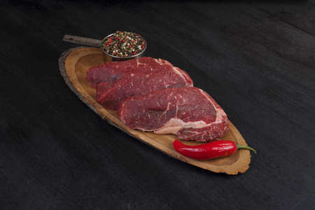 fresh raw beef piece fillet on middle size wooden plate with pepper and peppercorns in measuring spoon space for text on black backgroundの写真素材
