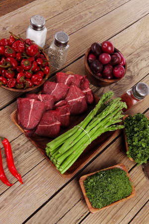 fresh beef meat asparagus greenery spices cutlery wooden table pepper crushed hot chili vegetables bowl servedの写真素材