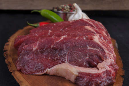 fresh raw beef pieces fillet on big size wooden plate with pepper and peppercorns in measuring spoon space for text on black backgroundの写真素材