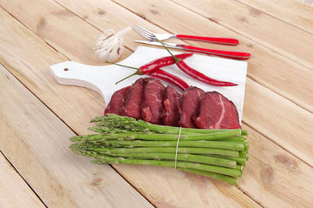 fresh beef meat slices asparagus spices cutlery wooden table pepper hot chili vegetables served garlic light cutting board ready to cookの写真素材