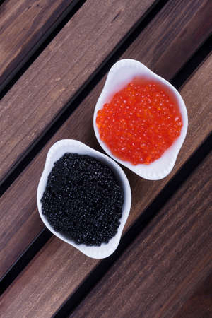 black sturgeon hausen caviar with red salmon caviar in white bowls on wooden backgroundの写真素材
