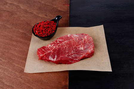 fresh raw beef rib eye steak on black walnut wooden table with red hot pepper spice in saucerの写真素材