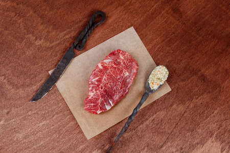 fresh raw beef rib eye steak on walnut table with salt spice and black iron antique forged cutlery fork knife empty space for textの写真素材