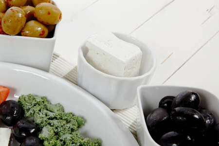 fresh greek feta cheese sandwich on white plate with hot green olives and black, goat cheese cube, tomatoes kale over retro tableの写真素材