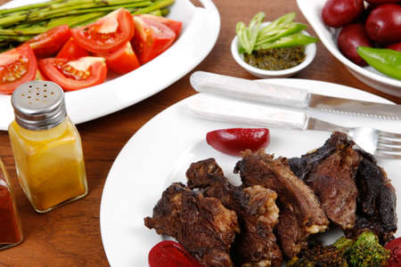 lunch of grilled meat served on big white plate with asparagus pickles tomatoes olives hot black red green pepper salt baked beans and ketchup on wooden tableの写真素材
