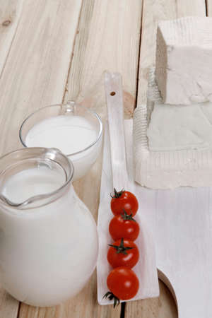 healthy dairy food fresh white greek goat sheep feta cheese on plate with milk in glass and full jug cherry tomatoes french bun over light wooden table with cutleryの写真素材