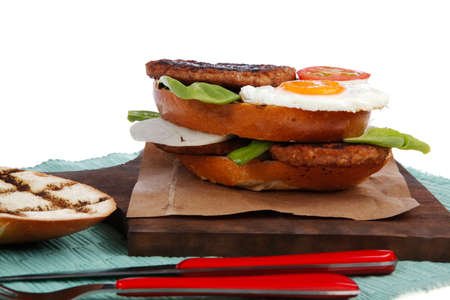 junk food big beef hamburger on dark wood plate with modern cutlery on blue mat isolated over white backgroundの写真素材