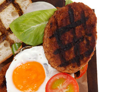 junk food big beef hamburger fried eggs on dark wood plate with modern cutlery isolated over white backgroundの写真素材