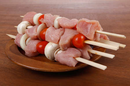 fresh raw meat fillet shish kebab turkey pork pink on skewers tomatoes mushrooms on wooden dish on big wood tableの写真素材