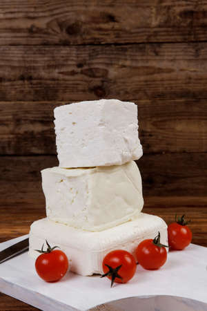 dairy healthy food fresh white greek goat sheep feta cheese on wood cutting plate with cherry tomatoes and french bun over dark wooden tableの写真素材