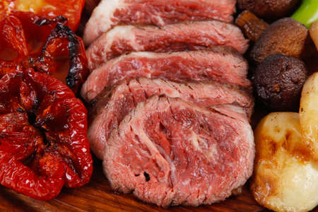 fresh grilled bbq beef meat rib eye steak on wooden plate with baked tomatoes mushroom, potatoes, hot chili pepper isolated on white backgrodunの写真素材