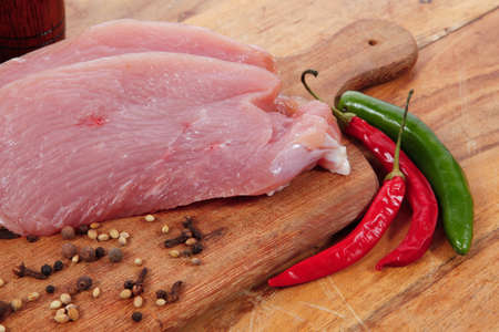 fresh raw turkey meat steak with hot sweet pepper dry spices castor and pepperbox on wood cutting boar over tableの写真素材