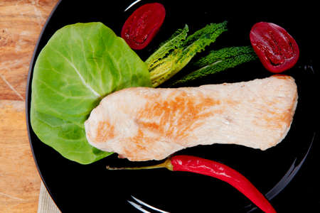 fresh roast turkey meat steak fillet with red hot pepper and green lettuce salad kale on black plate over wooden table with knife and forkの写真素材