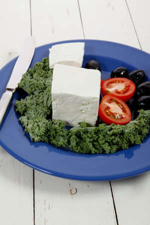 white goat feta cheese with black olives and tomatoes on blue plate over wooden tableの写真素材