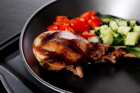 fresh hot grilled turkey drumstick leg with vegetables on black metal plate over wooden tableの写真素材