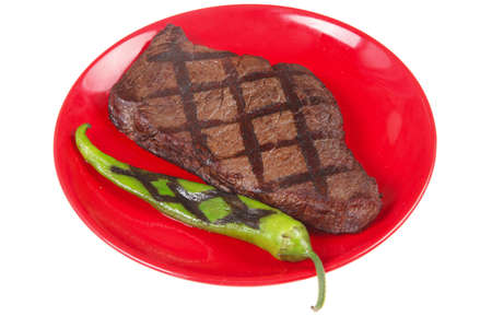 fresh grilled bbq roast beef steak on red plate with green chili pepper isolated on white backgroundの写真素材
