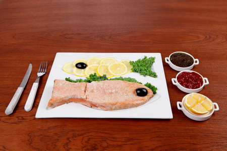 healthy food fresh roast red fish salmon with kale lemon antipesto ketchup sauce on white plate over wooden tableの写真素材