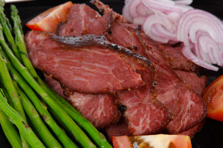 fresh sliced roast beef on black plate with cutlery and asparagus isolated on white backgroundの写真素材
