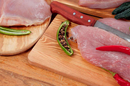 fresh raw turkey meat steak fillet with vegetables kale tomatoes lettuce red hot chili pepper and dark olives on cutting board over wooden tableの写真素材