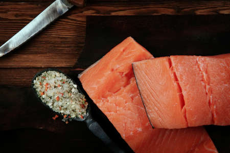 fresh raw salmon fillet served with lemon and white wine in wineglass, bottle, on dark plate over vintage wood table with handmade cutlery knife and spice on spoonの写真素材