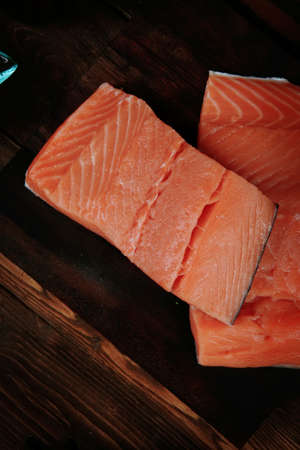 fresh raw salmon fillet served with lemon and white wine in wineglass, bottle, on dark plate over vintage wood table with handmade cutlery knife and spice on spoonの写真素材