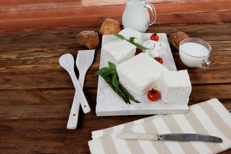 fresh white greek feta cheese with milk in jar basil cherry tomato asparagus and french bun on cutting board over dark wood table empty space for textの写真素材